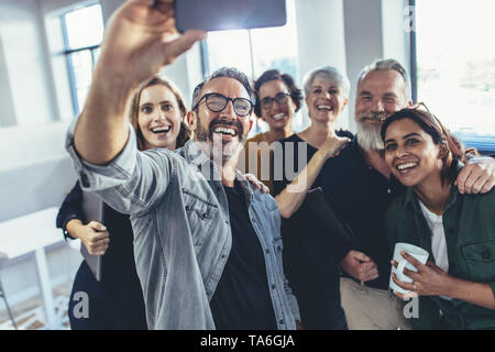 La gente di affari tenendo selfie con telefono e sorridente. Il successo del team aziendale tenendo selfie insieme in ufficio. Foto Stock