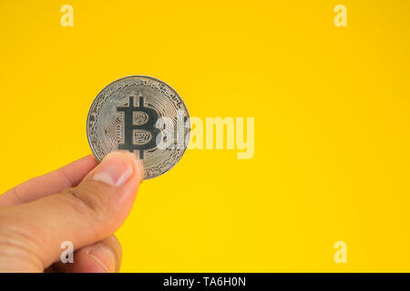Business man mano che tiene Bitcoin tra le dita su sfondo giallo. Valuta digitale, il blocco della catena, mercato business online Foto Stock