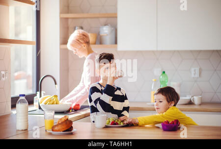 Una giovane donna con due bambini di mangiare la frutta in una cucina. Foto Stock