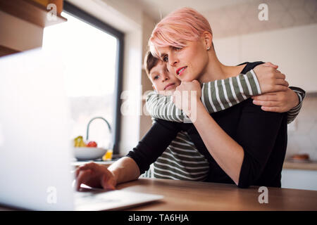 Una giovane donna con un piccolo figlio utilizzando computer portatile in una cucina a casa. Foto Stock