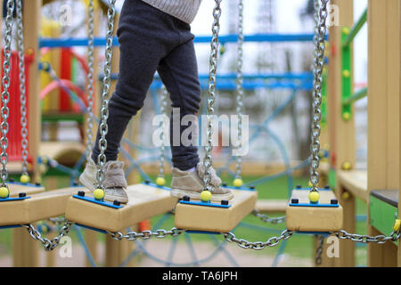 Bambino cammina su una sospesa per i bambini di strada della catena sul parco giochi Foto Stock