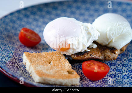 Uova Benedict con bistecca di carne, pomodori e toast giacente su una piastra di colore blu Foto Stock