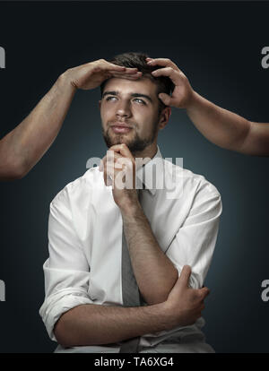 Un modello maschile circondato da mani come il suo pensiero su sfondo scuro. Un giovane uomo di dubbi, non riesco a scegliere la giusta decisione e sogni. Concetto di problemi mentali e disturbi nel lavoro, indecisione. Foto Stock