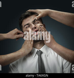 Un modello maschile circondato da mani come il suo pensiero su sfondo scuro. Un giovane uomo di dubbi, non riesco a scegliere la giusta decisione e decidere. Concetto di problemi mentali e disturbi nel lavoro, indecisione. Foto Stock