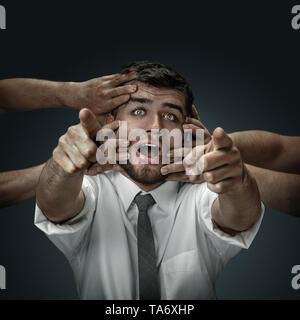 Un modello maschile circondato da mani come il suo pensiero su sfondo scuro. Un giovane uomo di dubbi, non riesco a scegliere la giusta decisione e decidere. Concetto di problemi mentali e disturbi nel lavoro, indecisione. Foto Stock