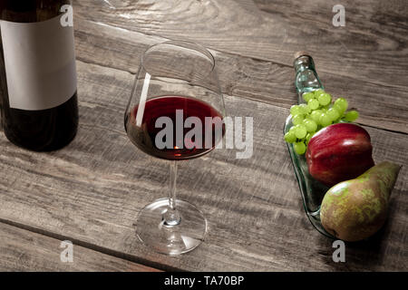 Delicisious e gustosi cibi e bevande. Una bottiglia e un bicchiere di vino rosso con frutti più weathered sfondo di legno. Vista da sopra con copia spazio per inserire il vostro annuncio. Uva, mela, pera e tappi in sughero. Foto Stock