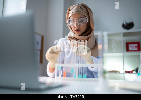 Giovane farmacista indossando i guanti lavora con le provette per la prova Foto Stock