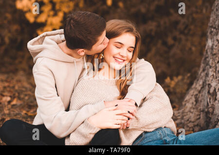 Felice amore giovane og adolescenti seduto sotto agli alberi all'esterno. Ragazzo baciare ragazza. Teenagerhood. Foto Stock