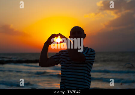 le mani maschili sotto forma di cuore contro il cielo passano raggi solari. Mani in forma di cuore d'amore Foto Stock
