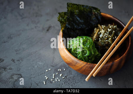Tradizionale snack giapponese - Chuka alghe wakame insalata croccante e arrosto di nori fogli in ciotola di legno su sfondo scuro vista superiore con spazio di copia Foto Stock
