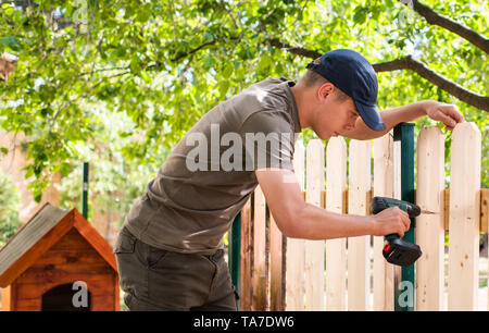 Giovane uomo bello utilizzando un trapano elettrico sulla recinzione di legno Foto Stock