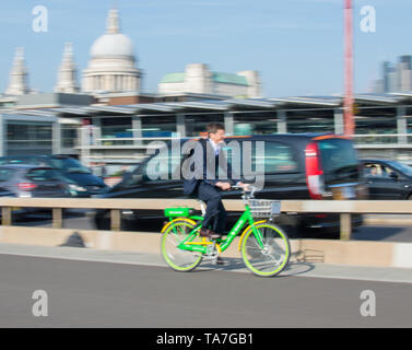 Un uomo vestito in sella ad una condivisione elettrico bike a calce e in motion blur su Blackfriars Station con St.Pauls sullo sfondo Foto Stock