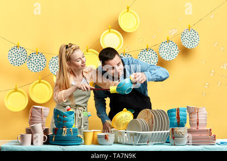 Curioso l uomo e la donna in cerca di sport, la polvere in kitchenwear in cucina con parete gialla. close up foto Foto Stock
