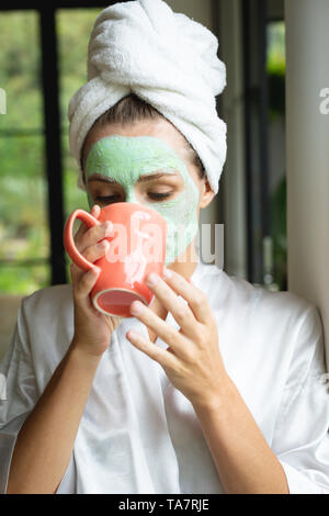 Donna in maschera facciale di bere il caffè a casa Foto Stock