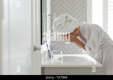 La donna il lavaggio la sua maschera facciale nel lavandino del bagno a casa Foto Stock