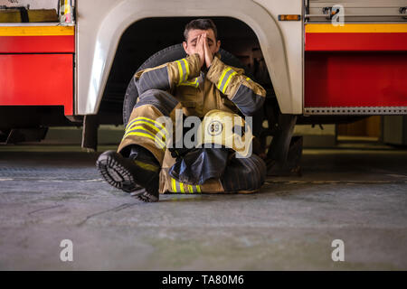 Foto di stanchi fireman seduto sul pavimento vicino al red fire carrello in corrispondenza della stazione Foto Stock