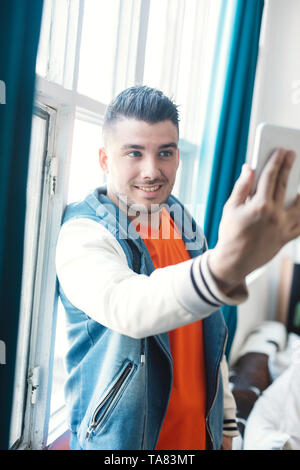 Un sorridente bel giovane uomo prendendo Self immagine utilizzando il telefono cellulare all'interno dell'Aula. Foto Stock