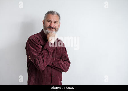 A mezza lunghezza Ritratto di un grave grey-haired uomo barbuto in una maglietta di borgogna su uno sfondo bianco. Foto Stock
