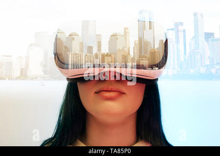 Doppia esposizione di bruna ragazza indossando la realtà virtuale auricolare e città moderna con grattacieli Foto Stock