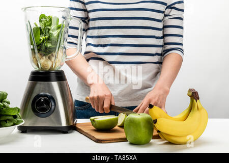 Vista ritagliata della donna il taglio di Apple nei pressi di Blender e di banane su bianco Foto Stock