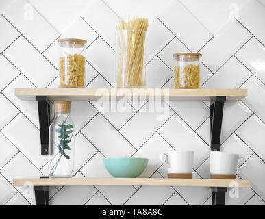 Cucina in legno Scaffali con tazze e vasetti di vetro sul muro bianco Foto Stock