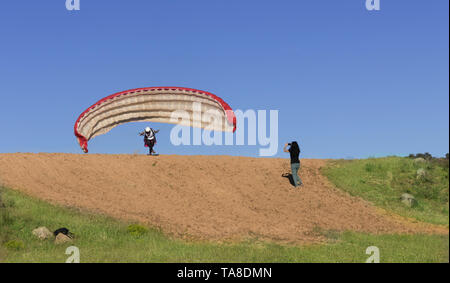 Femmina pilota di parapendio in decollo e la donna le riprese con il suo mobile, con un cielo blu in background Foto Stock