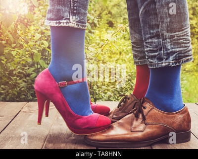 Gli uomini e le donne per le gambe in scarpe alla moda, luminoso, multi-colore di calze su una terrazza in legno sullo sfondo di verdi alberi e raggi di sole. Close-up Foto Stock