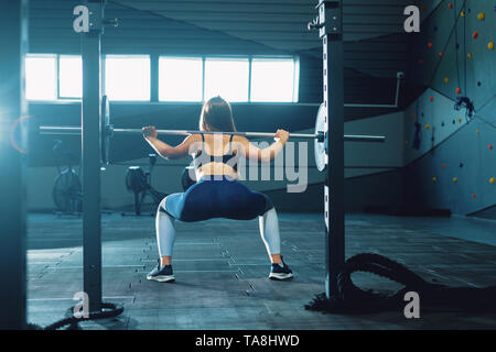 Ragazza ginnasta facendo squat barbell. Vista frontale di attraente giovane donna Foto Stock