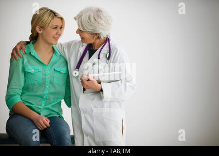 Donna sorridente medico avente una discussione con un giovane paziente di sesso femminile dentro un ambulatorio medico. Foto Stock