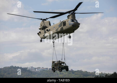 Un U.S. Esercito CH-47 elicottero Chinook, assegnato al Bravo Company, 2° Battaglione, 1a combattere la Brigata Aerea, 1a divisione di fanteria, conduce un assalto dell'aria missione con un esercito di mobilità di massa veicolo (AGMV) sling caricato con i paracadutisti assegnato alla società di attacco, 1° Battaglione, 503rd Reggimento di Fanteria, 173rd Brigata Aerea, caricati a bordo durante l'esercizio una risposta immediata a Vojarna Josip Jovic Airbase, Udbina, Croazia, 17 maggio 2019. Esercizio risposta immediata è un esercizio di multinazionale co-guidato dal croato di Forze Armate, Sloveno Forze Armate, E DEGLI STATI UNITI Esercito europeo. La logistica-focalizzata Foto Stock