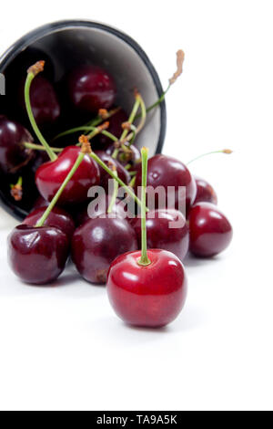 Tazza bianca con bacche mature di Rosso ciliegio dolce e diverse bacche nella parte anteriore della tazza. Composizione su uno sfondo bianco. Foto Stock