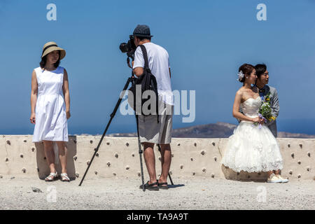 Santorini, i turisti al di sopra del mare sulla terrazza, uomo che fa foto con treppiede. Appena si sposavano giovani popoli asiatici, Grecia Europa Foto Stock