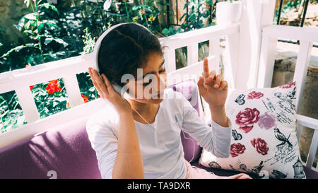 Bambina ascoltando musica, godendo la melodia sul divano. Ha posti a sedere fuori in giardino, indossando le cuffie. Foto Stock