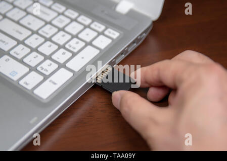 Mano umana l'inserimento di una scheda SD nel personal computer portatile Foto Stock