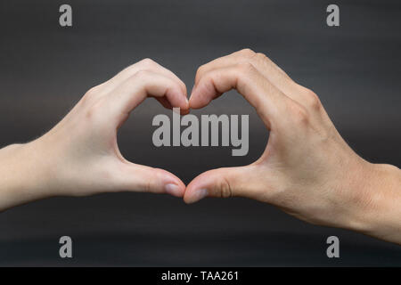 Le mani a forma di cuore su sfondo nero Foto Stock