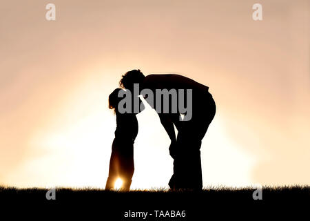 Una silhouette di una bambina bambino baciare suo padre al tramonto di un giorno d'estate. Foto Stock