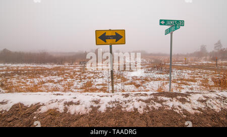 Segnaletica stradale e freccia(s) segno - sezione trasversale di due zone rurali strade di ghiaia in Wisconsin settentrionale - freddo inverno nevoso giorno nella prateria / prairie / fr Foto Stock