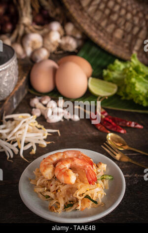 Thai noodles fritti o pad thai con gamberi sulla piastra bianca collocato sul tavolo di legno sono forchetta, cucchiaio, uova, lattuga, aglio, germogli di soia, argento Foto Stock