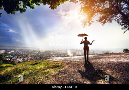 Silhouette di donna con ombrello la strada con vista sul panorama della città in piovoso tramonto spettacolare . Vintage, in stile retrò. Foto Stock