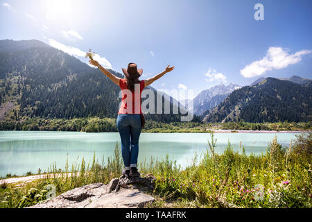 Tourist donna con cappello in salita e il cappello da cowboy godendo di una splendida vista del lago di montagna in Kazakistan Foto Stock