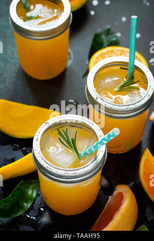 Rinfrescanti cocktail estivi fatti di agrumi e di mango, bevanda fredda con ghiaccio su una pietra scura sullo sfondo. Concetto di vitamine fresco. Stile rustico. Foto Stock