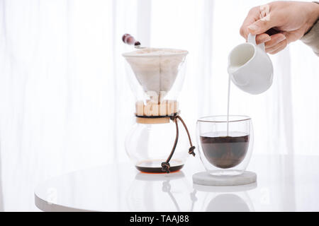 L'uomo versando il latte in vetro con il freddo a preparare il caffè sul tavolo Foto Stock