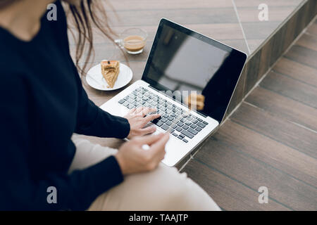 Vista aerea della giovane donna che lavorano sul suo computer portatile presso una caffetteria. Vista Top Shot della donna seduta al tavolo con una tazza di caffè navigando su internet. Foto Stock