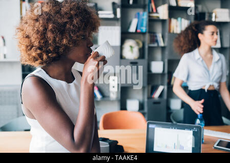 Due giovani imprenditrici multirazziale avente una riunione informale in un moderno ufficio coworking - interazione, creatività, pieni di risorse Foto Stock