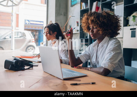 Due giovani donne e multirazziale lavorando su un progetto in un ufficio coworking, cooperazione - web design, creatività Foto Stock