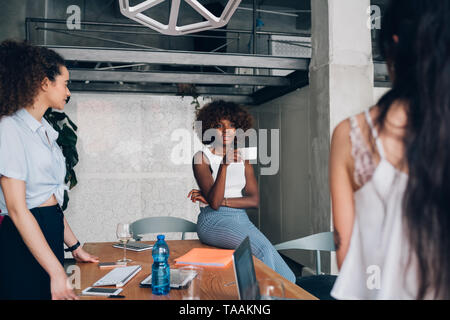 Tre giovani multirazziale freelancer donna avente una riunione informale in coworking office - interazione, creatività, tecnologia Foto Stock