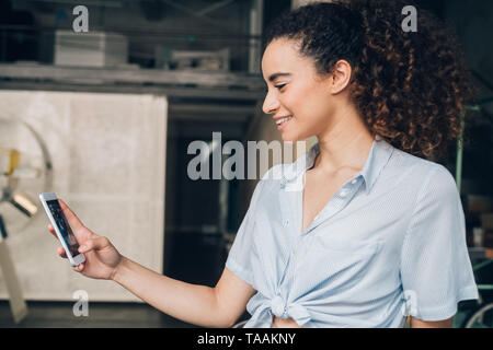 Giovane donna caucasica utilizza lo smartphone in moderni loft - gioventù, allegro, pieni di risorse Foto Stock