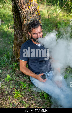 Fiducioso uomo rilascia una nube di vapore. Sigaretta elettronica concetto. Foto Stock