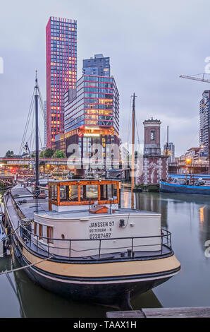 Rotterdam, Paesi Bassi, 21 Maggio 2019: Wijnhaven del porto al tramonto con una chiatta storica e sullo sfondo la mela rossa torre residenziale Foto Stock