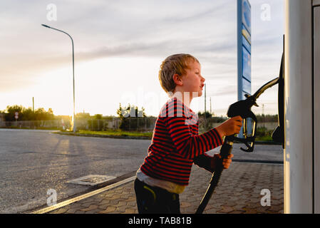 Bambino tenere il tubo di una pompa del carburante al tramonto in corrispondenza di una stazione di gas. Foto Stock